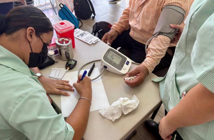 Personal de salud anota resultados mientras un hombre recibe la medición de presión arterial con un monitor digital durante la jornada del DIF.
