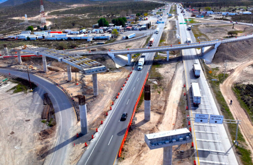 Cruce vial en construcción donde la Carretera Interserrana se conecta con una autopista, con puentes y tráfico de carga.