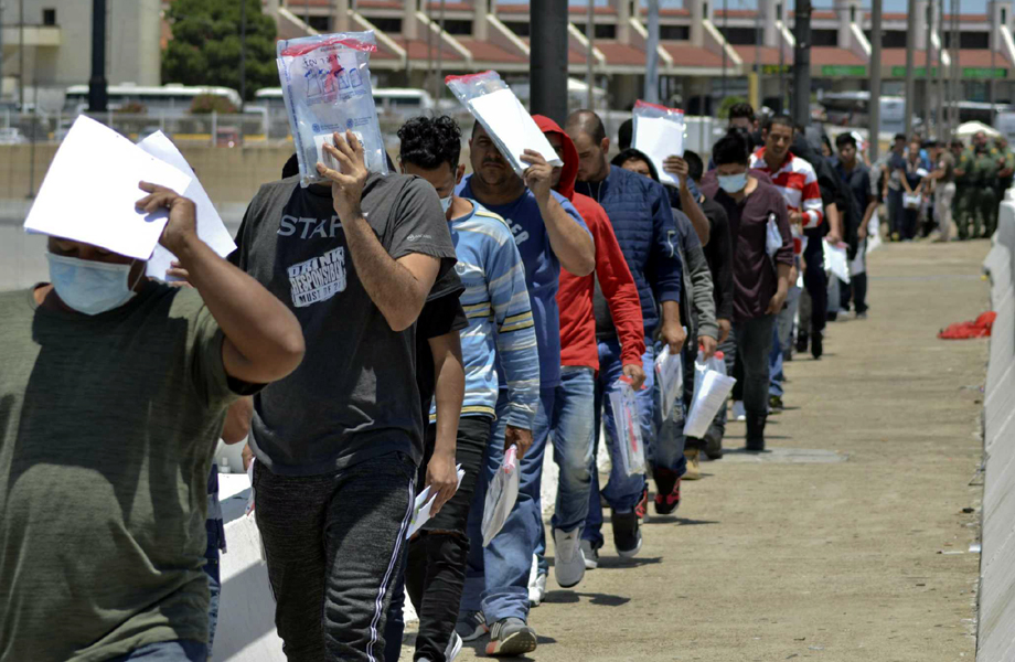 Personas repatriadas caminan en fila con documentos oficiales en un cruce fronterizo hacia México