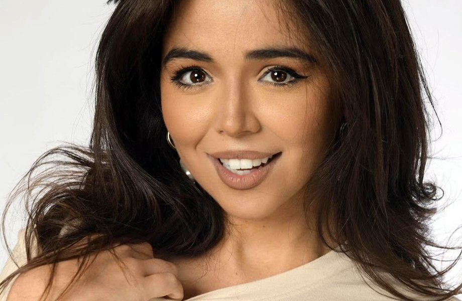 Retrato de una mujer joven con expresión amistosa, cabello suelto y maquillaje natural en un fondo blanco.