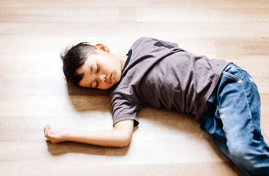 Niño desmayado en el piso durante una emergencia doméstica que requiere primeros auxilios.