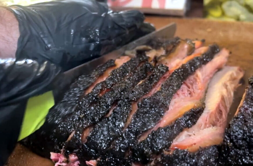 Brisket ahumado siendo rebanado sobre una tabla, con corteza oscura y carne jugosa en primer plano
