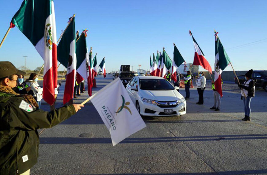 Funcionarios y voluntarios ondean banderas mexicanas para recibir a paisanos que regresan en caravana durante el operativo decembrino en la frontera.