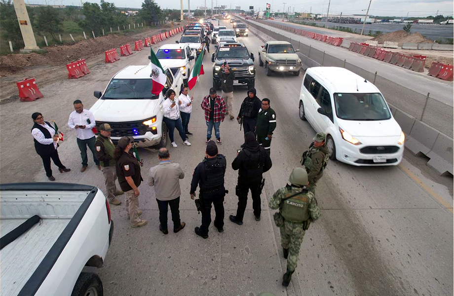 Vehculos autoridades y personal de apoyo organizan el arranque de una caravana de migrantes en una vialidad cercana a la frontera
