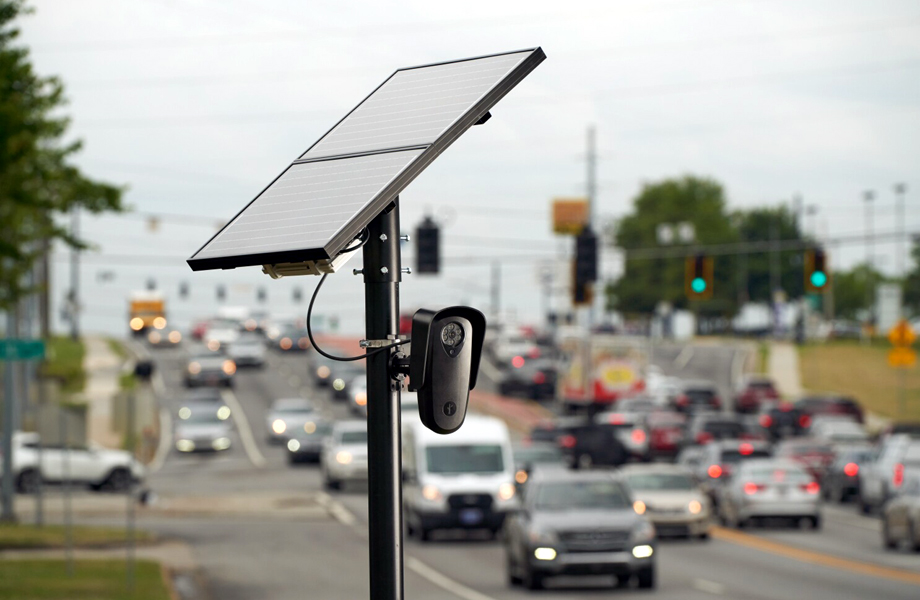 Lector automático de placas con panel solar instalado junto a una avenida concurrida para monitorear el tráfico.