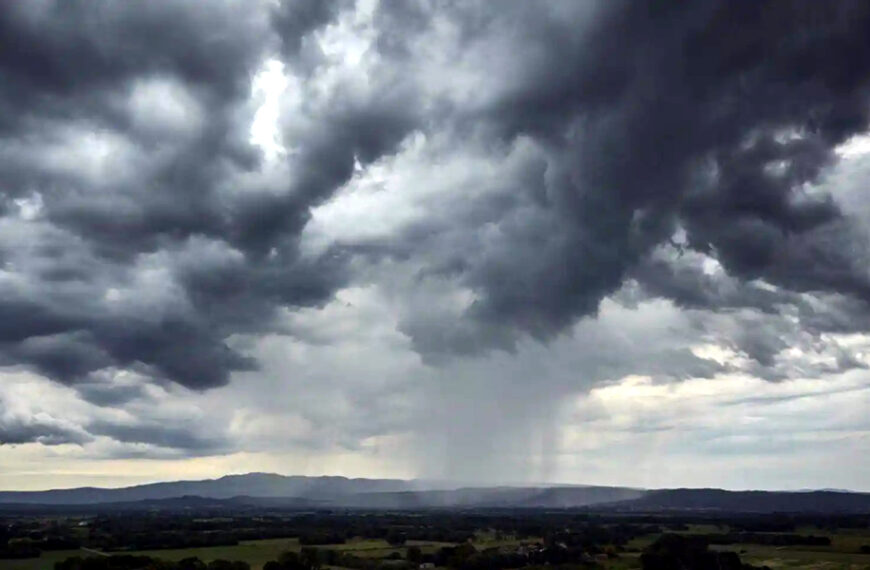 Cielo oscuro con nubes de tormenta y una columna de lluvia cayendo a la distancia sobre un paisaje rural