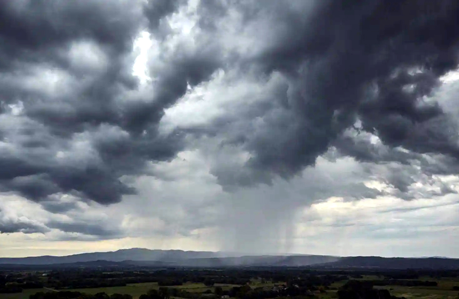 Cielo oscuro con nubes de tormenta y una columna de lluvia cayendo a la distancia sobre un paisaje rural