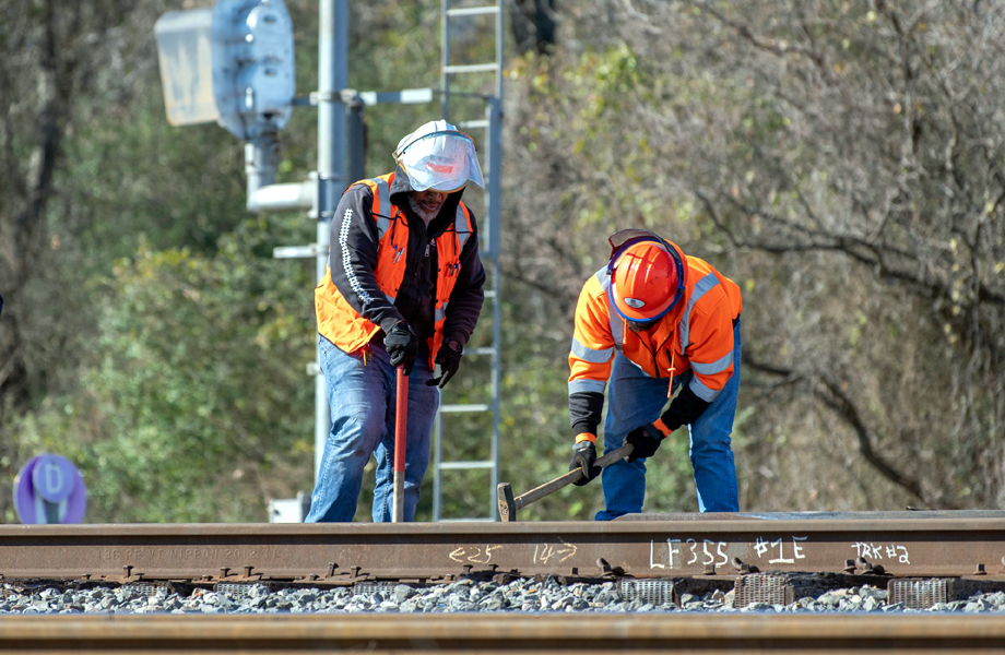 Trabajadores ferroviarios con chaleco naranja ajustan rieles de acero en una vía en construcción