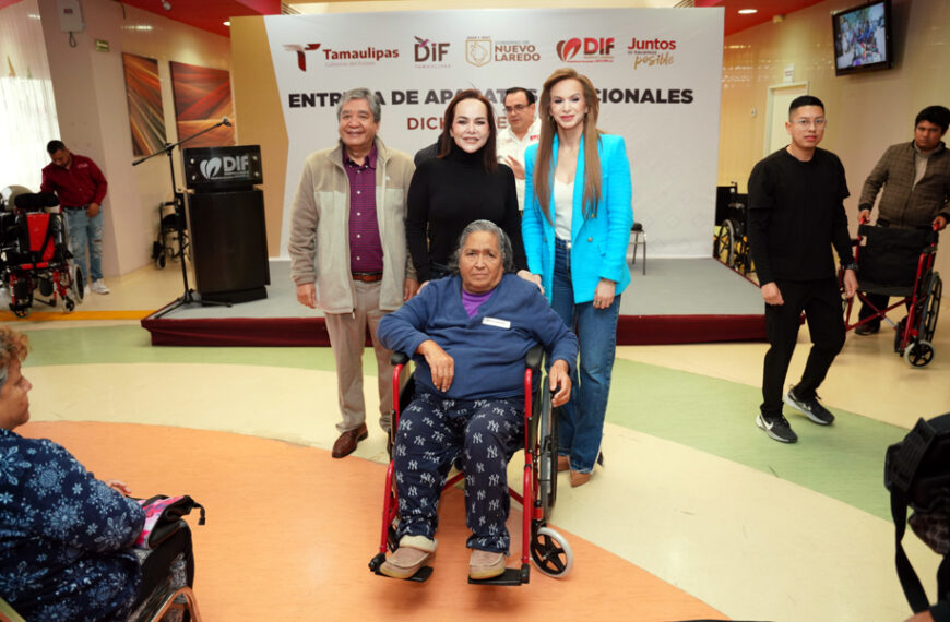 Mujer adulta mayor en silla de ruedas recibe apoyo de aparatos funcionales mientras autoridades del DIF Nuevo Laredo la acompañan frente al escenario del CRI.