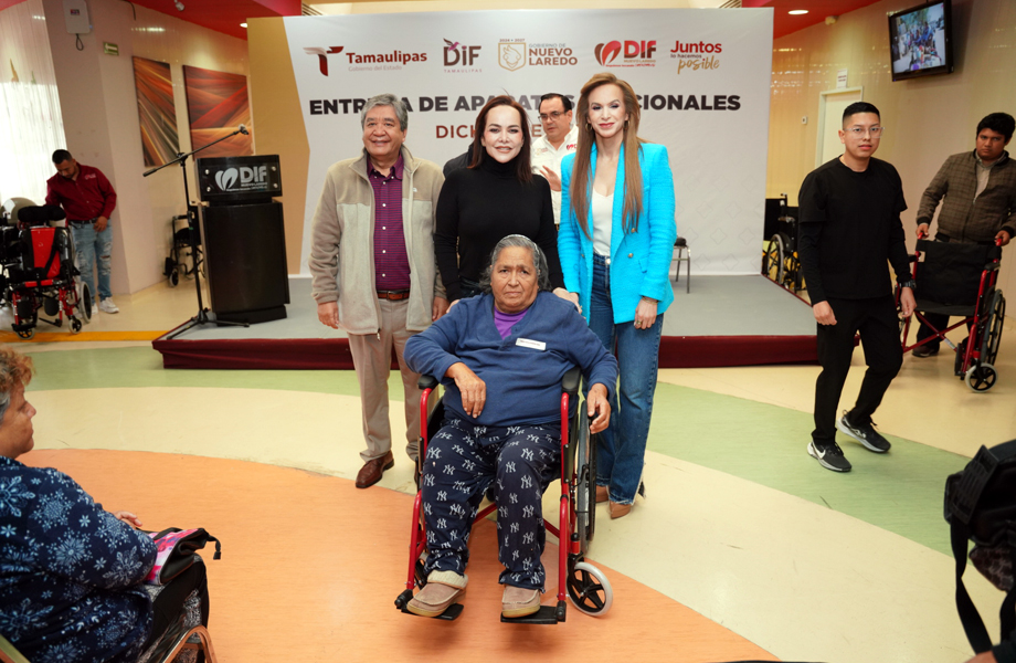 Mujer adulta mayor en silla de ruedas recibe apoyo de aparatos funcionales mientras autoridades del DIF Nuevo Laredo la acompañan frente al escenario del CRI.