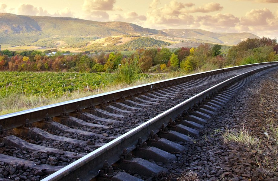 Vas de tren que se pierden en la distancia entre campos verdes y colinas bajo un cielo parcialmente nublado