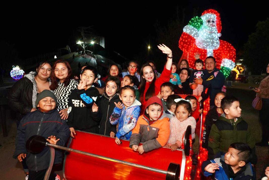 Grupo de nias y nios dentro de un trineo rojo posando con la alcaldesa frente a una figura gigante de Santa Claus iluminado