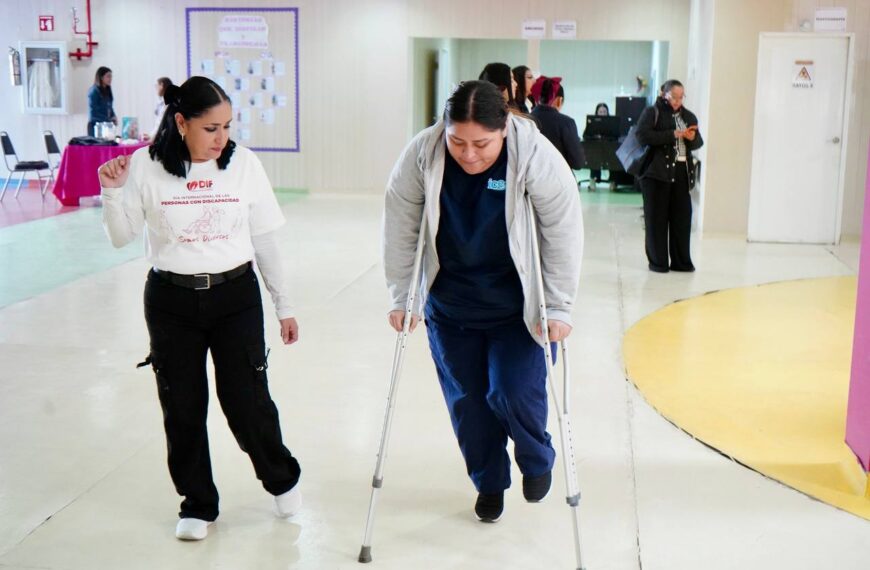 Mujer camina con muletas guiada por personal del DIF como parte de una dinámica de sensibilización sobre discapacidad motriz.