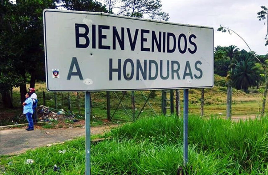 Letrero carretero con la frase “Bienvenidos a Honduras” rodeado de vegetación, en una zona fronteriza.