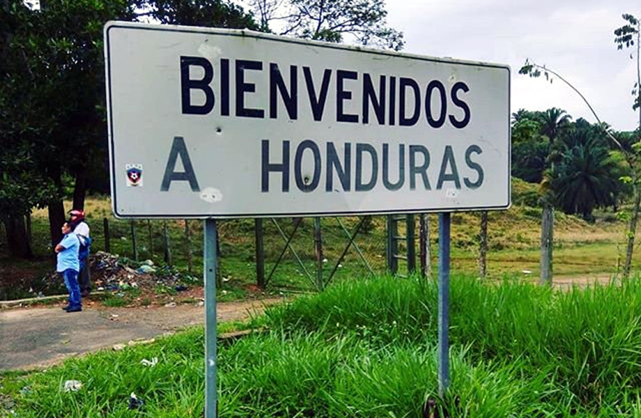 Letrero carretero con la frase “Bienvenidos a Honduras” rodeado de vegetación, en una zona fronteriza.