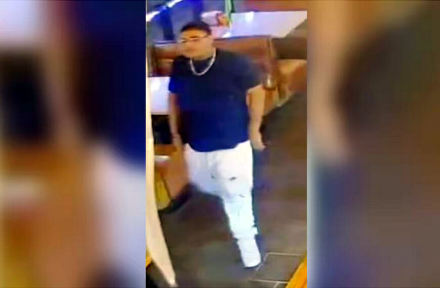 Fotografía de cámara de seguridad que muestra a una persona de interés para la Policía de Laredo, un hombre joven con playera oscura y pantalón claro, caminando dentro de un establecimiento.