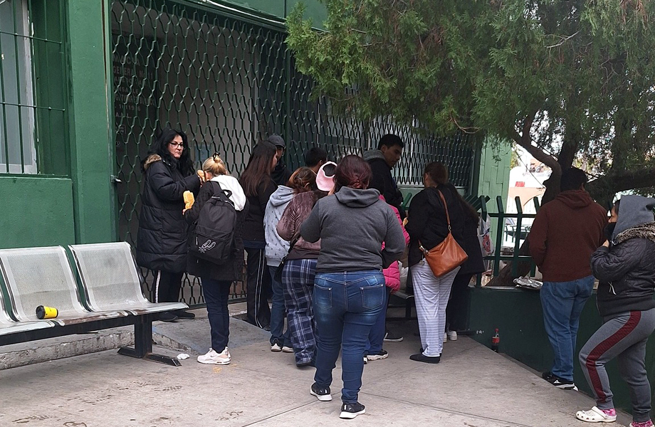 Grupo de derechohabientes abrigados haciendo fila junto a bancas metlicas frente a una reja cerrada del hospital del IMSS en Nuevo Laredo