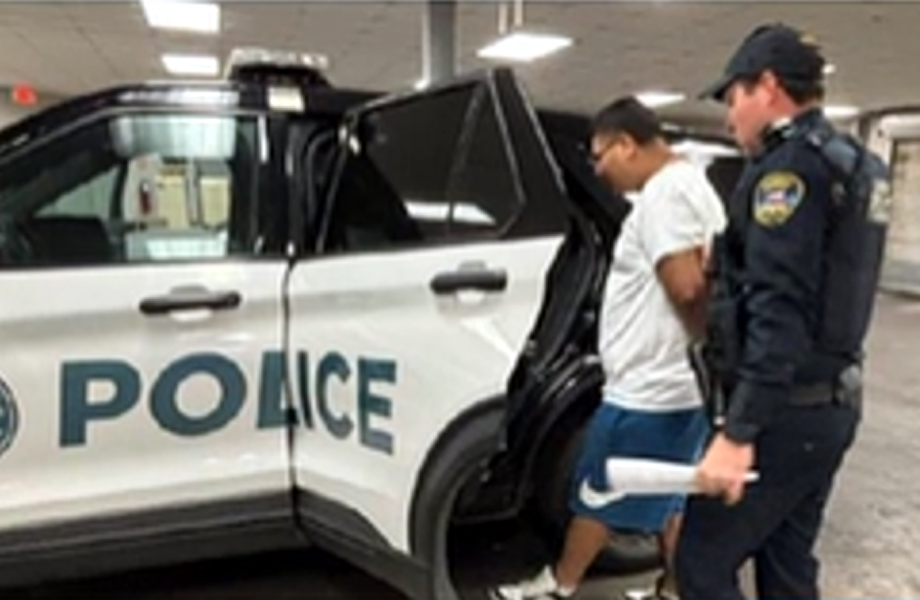 Oficial de la Polica de Laredo acompaa a un hombre esposado hacia la parte trasera de una patrulla blanca y negra en un rea techada