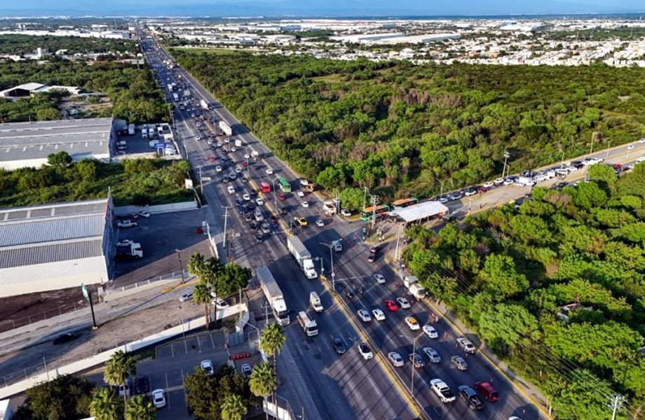 Carretera urbana con trfico intenso de trileres y autos junto a zona industrial y rea verde