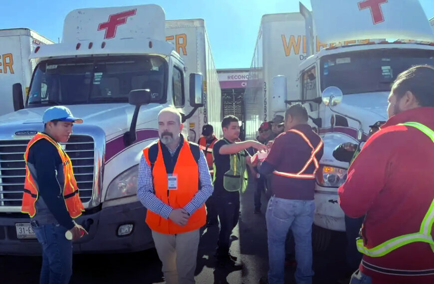 Choferes y personal de logística con chalecos reflejantes frente a tráileres alineados en un cruce fronterizo.