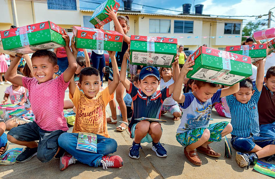 Nios sentados al aire libre levantando cajitas de regalo de Samaritans Purse y sonriendo a la cmara