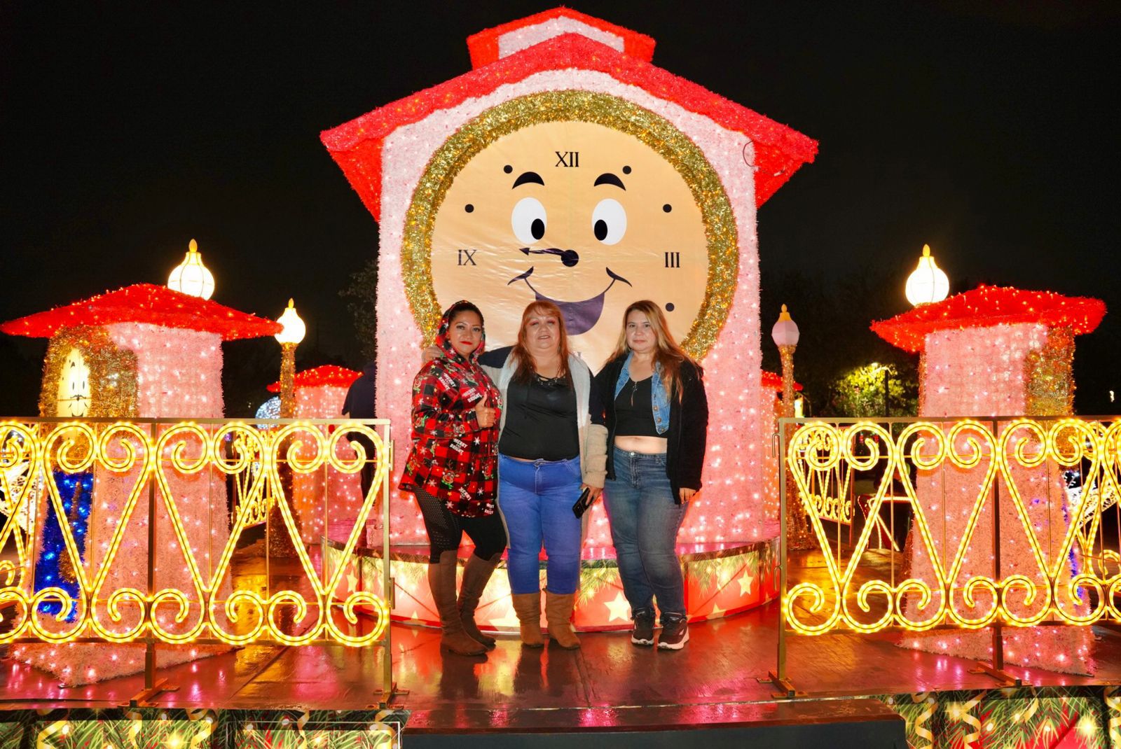 Tres mujeres posan frente a un reloj monumental iluminado como parte del recorrido navideño en El Viveros Mágico.