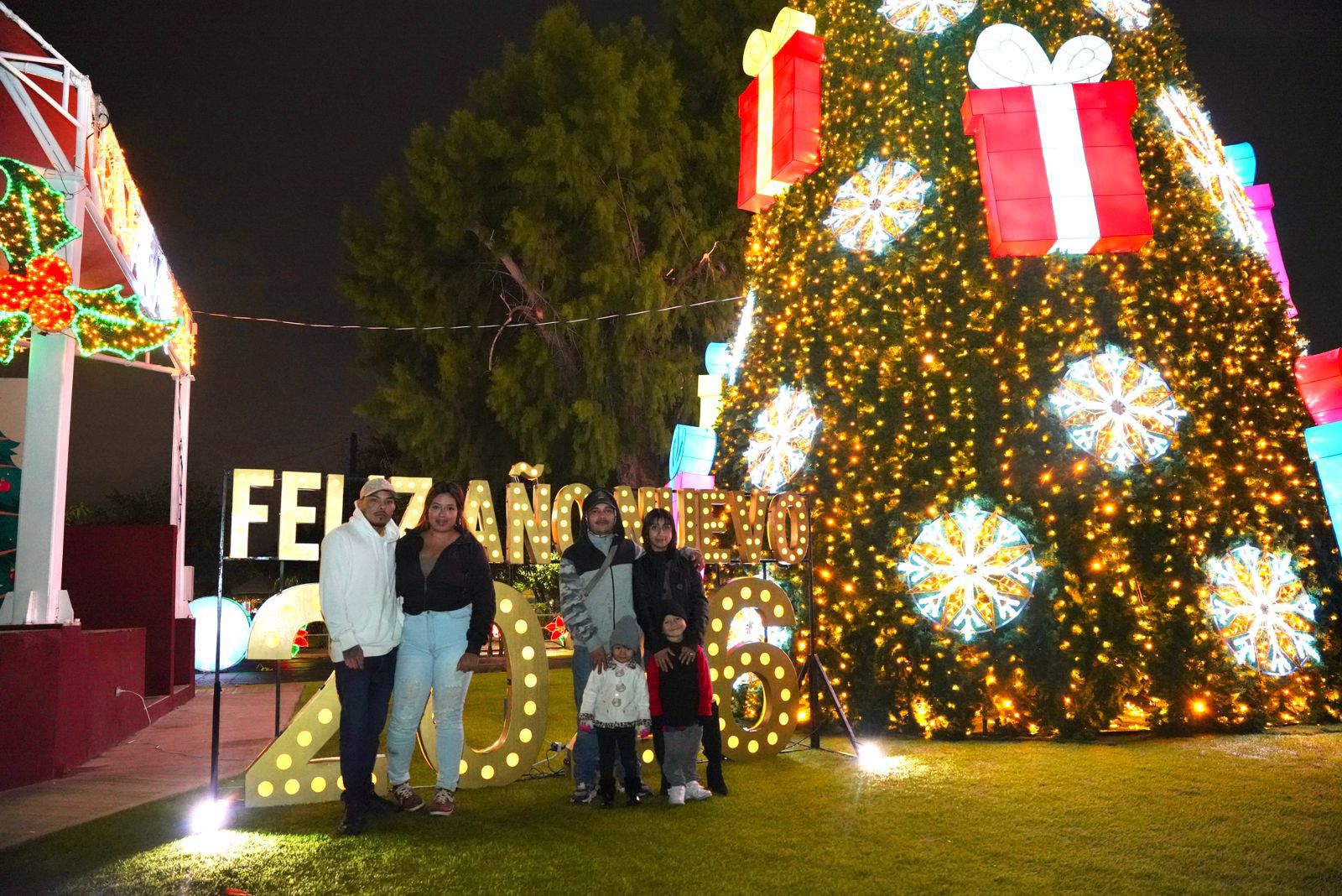 Familia posa junto al letrero 2026 y un rbol navideo iluminado durante el recorrido de El Viveros Mgico en Nuevo Laredo