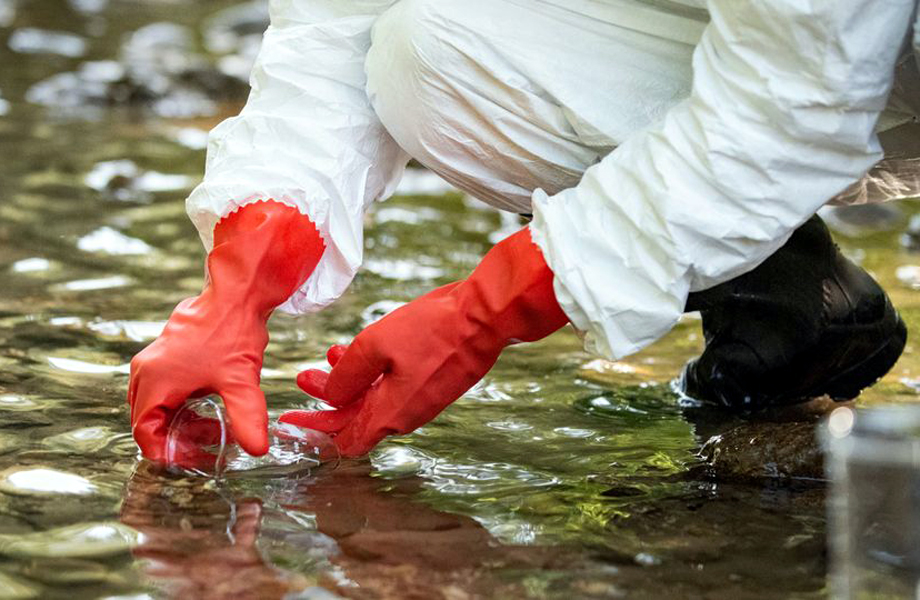 Tcnico con equipo de proteccin recolectando muestra de agua para anlisis epidemiolgico y deteccin de virus