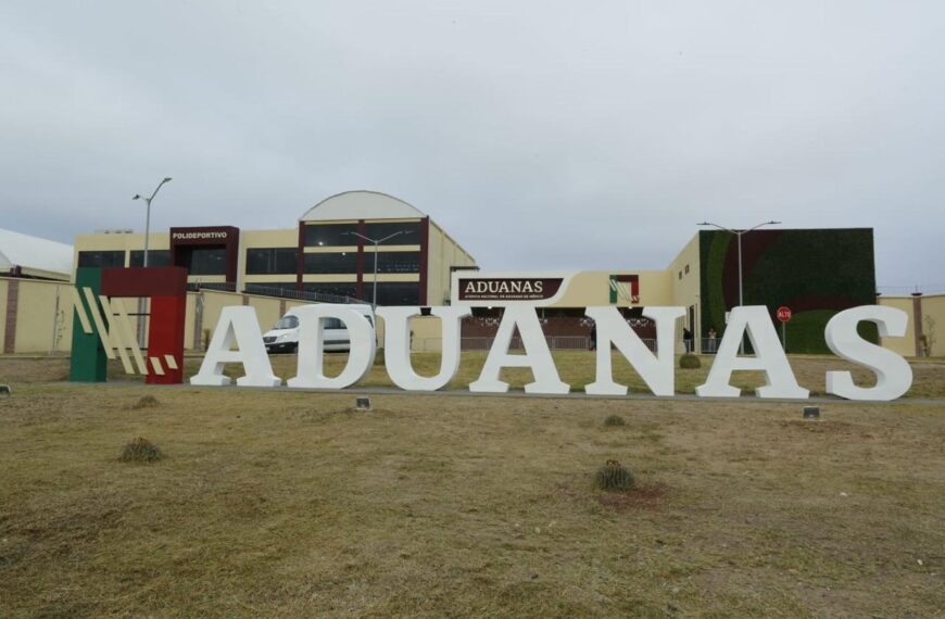 Vista frontal del complejo de la Agencia Nacional de Aduanas de México en Nuevo Laredo, con letras monumentales y áreas verdes frente a las instalaciones.