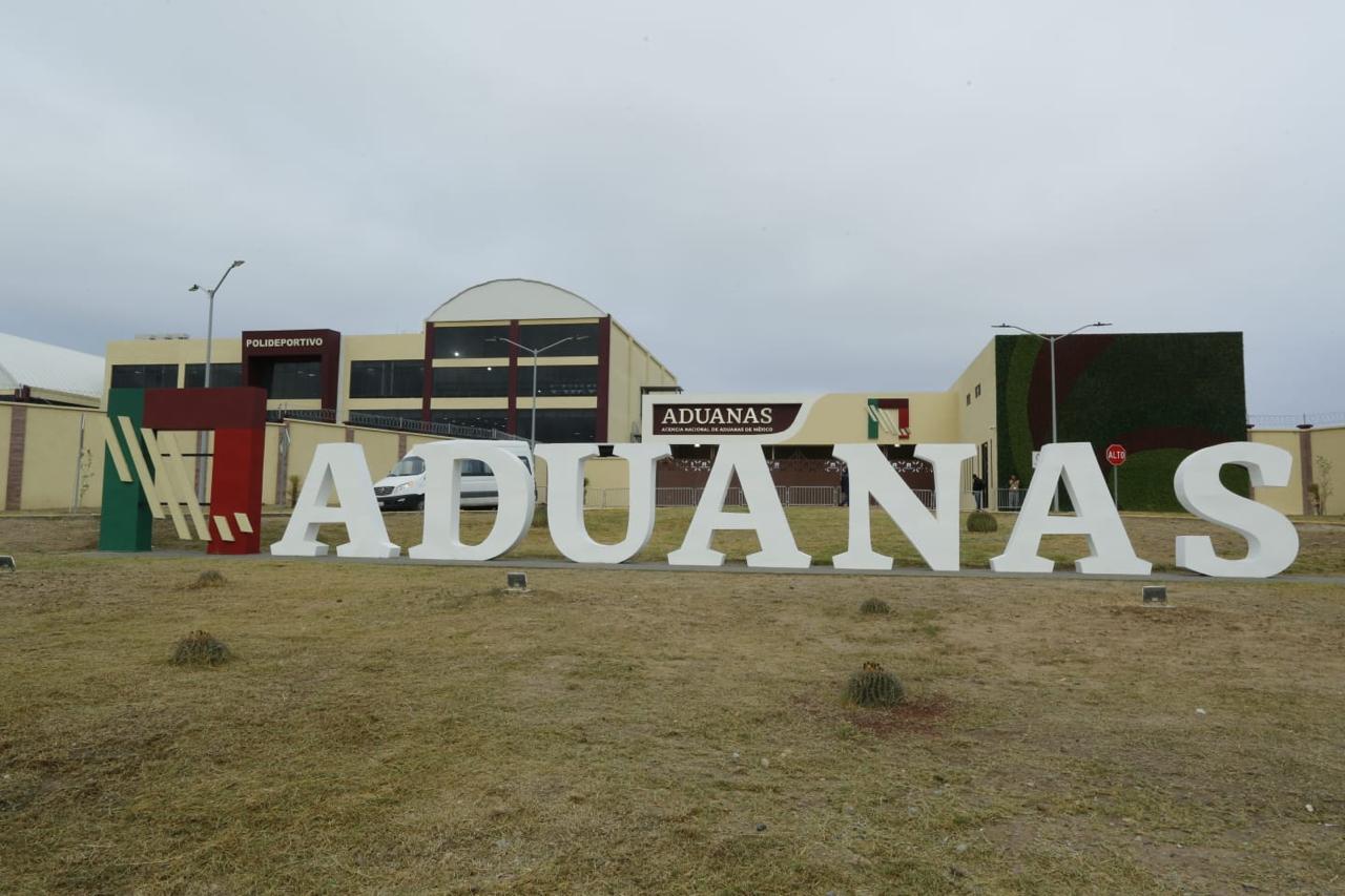 Vista frontal del complejo de la Agencia Nacional de Aduanas de México en Nuevo Laredo, con letras monumentales y áreas verdes frente a las instalaciones.