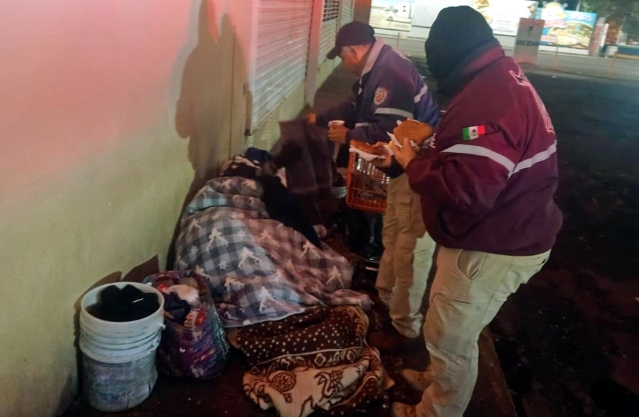 Personal de Protección Civil y Bomberos de Nuevo Laredo entrega cobijas, pan y café a una persona en situación de calle durante el Operativo Carrusel por bajas temperaturas.