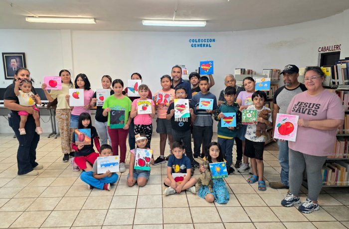 Group of children and adults in a library posing with colorful heart drawings held up for the camera.