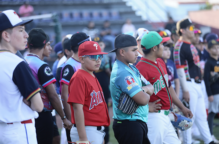 Group of young baseball players lined up on a field, wearing colorful uniforms and caps, waiting for the start of a game or ceremony.