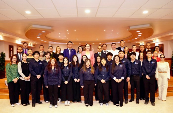 Group photo of a diverse team in matching dark shirts posing on a staged area in a warm-lit conference hall/atrium.