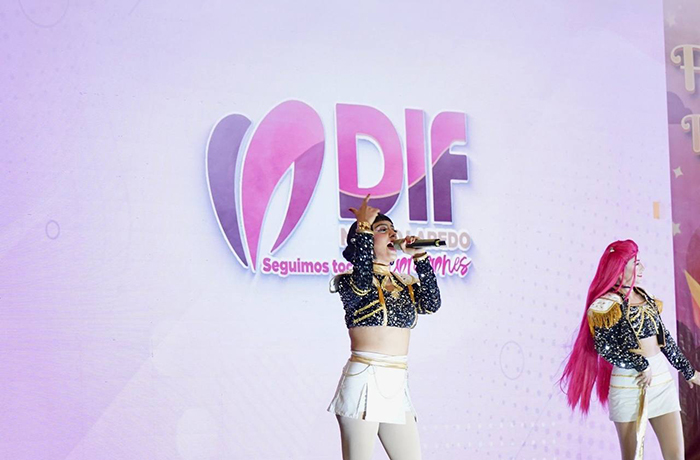 Two female performers sing and dance on a pastel pink stage with a large DIF logo backdrop behind them.