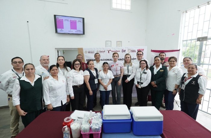 Group of health workers posing in a clinic during a national vaccination campaign; coolers and medical supplies on a table in the foreground.