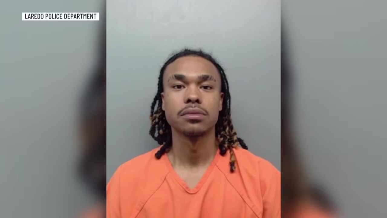 Mugshot of a man with braided hair wearing an orange jail jumpsuit against a gray wall, Laredo Police Department label visible on top left.