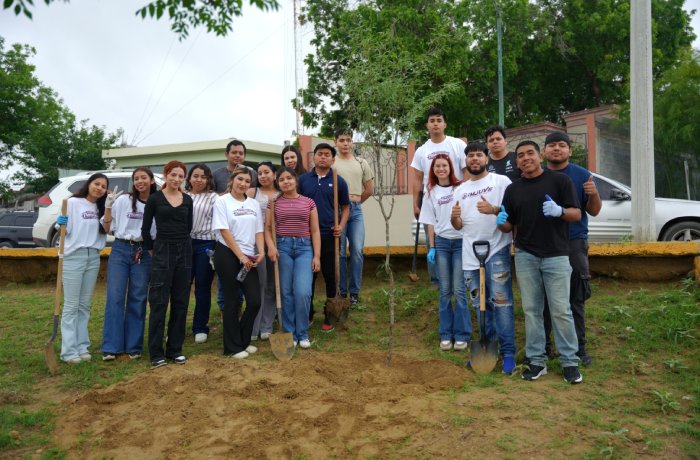Group of diverse volunteers posing with shovels beside a newly planted sapling during a tree-planting event in a park area