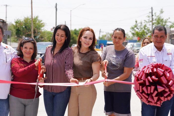 Group of people at a ribbon-cutting ceremony on a sunny street, holding a pink ribbon and scissors with a large pink bow nearby.