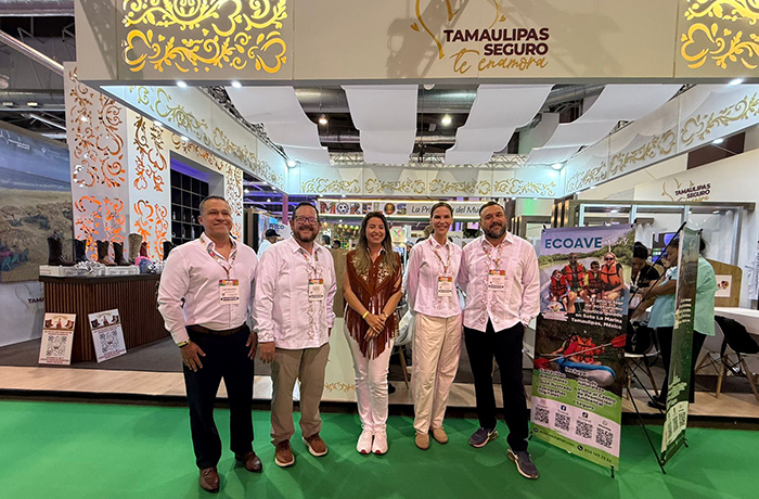 Six professionals stand together in front of a Tamaulipas booth at a trade show, featuring ornate white-and-gold decor and a bright green floor.