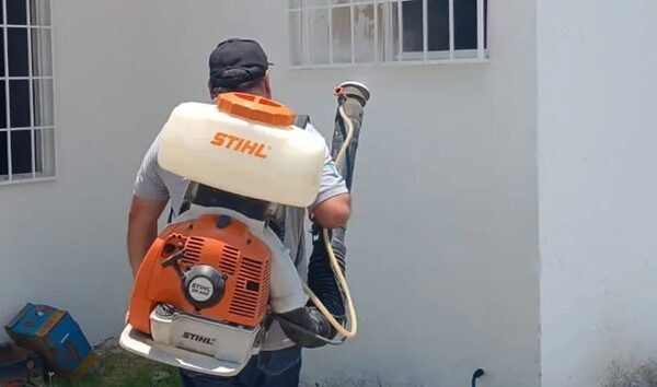 Worker wearing a STIHL backpack sprayer and holding the hose, ready to spray near a white wall.