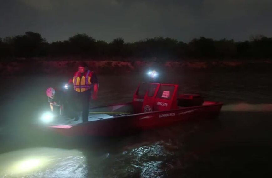 Red rescue boat on a dark river at night, two crew members in life jackets with bright headlights aiding a night rescue operation.