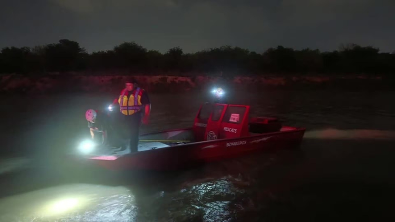 Red rescue boat on a dark river at night, two crew members in life jackets with bright headlights aiding a night rescue operation.