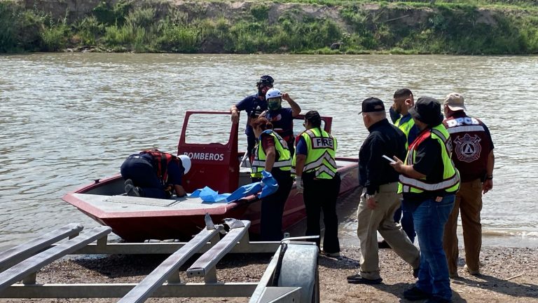 Firefighters and rescuers loading a small red boat labeled BOMBEROS onto a riverbank, wearing high-visibility vests.