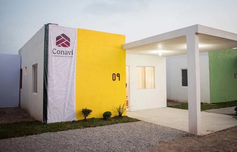 A modern white building with a bright yellow wall marked with the number 09 and a Conavi logo at the front entrance, with a covered walkway.