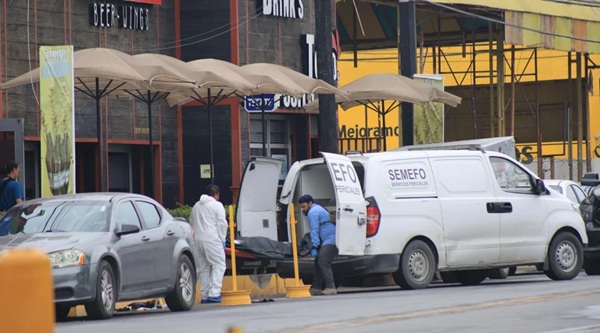 White vans parked on a city street with their back doors open and workers unloading under beige canopies; storefronts line the background.