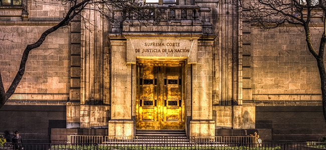 Golden doors of the Supreme Court of Justice of the Nation, illuminated entrance with stone facade at night.