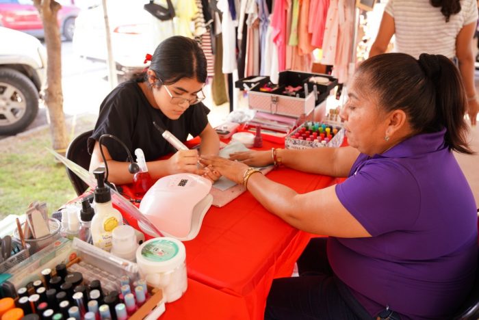 Nail technician applying polish to a woman's nails at an outdoor market manicure booth with polish bottles nearby