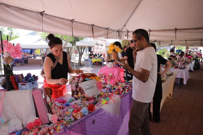 Vendor under a tent selling colorful handmade crafts to a man browsing at a market stall.