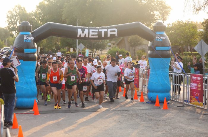 Runners burst from the starting line under a META inflatable arch, with spectators, barriers, and orange cones lining the road.